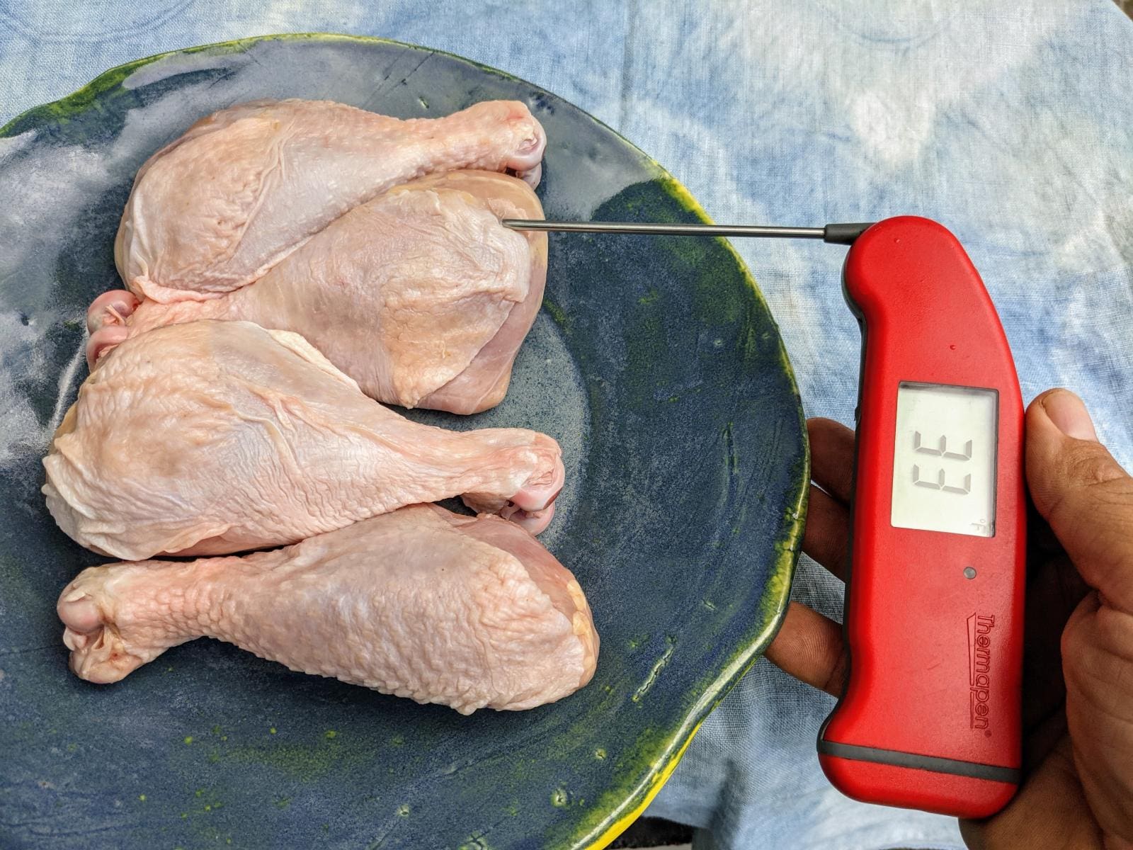 Using an instant read thermometer to check the level of defrosting in four pasture raised chicken breasts.