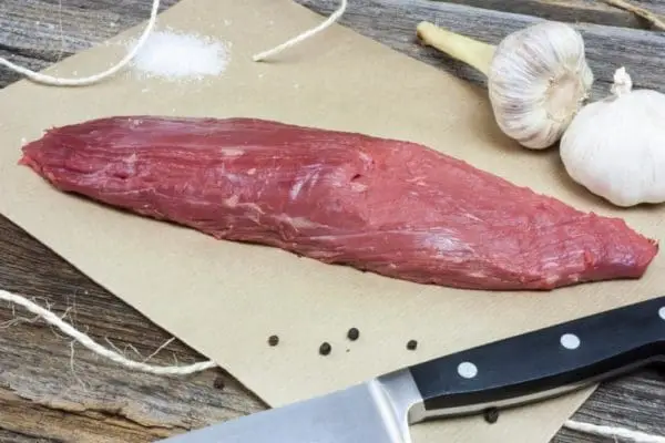 Grass Fed Beef Petite Tender on brown paper with garlic, salt, and peppercorns