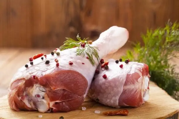 Pasture raised, Certified Organic turkey drumsticks from Wrong Direction Farm. On a cutting board garnished with peppercorns and herbs.