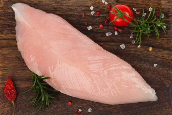 One Certified Organic, pasture raised turkey tenderloin from Wrong Direction Farm on a dark wood cutting board with salt, tomato, and rosemary.