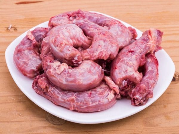 Certified Organic and Pasture Raised chicken necks from Wrong Direction Farm. Neck are shown raw and placed on a white plate.