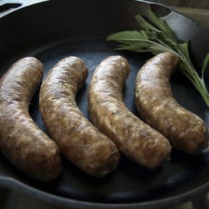 Four mild Italian sausages made with pasture raised pork in a cast iron pan.