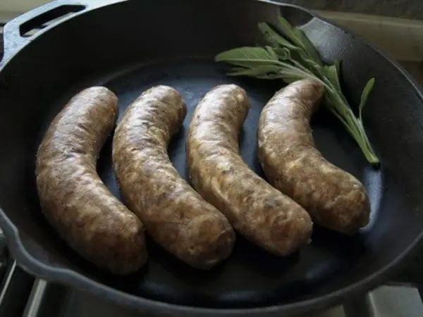 Four mild Italian sausages made with pasture raised pork in a cast iron pan.