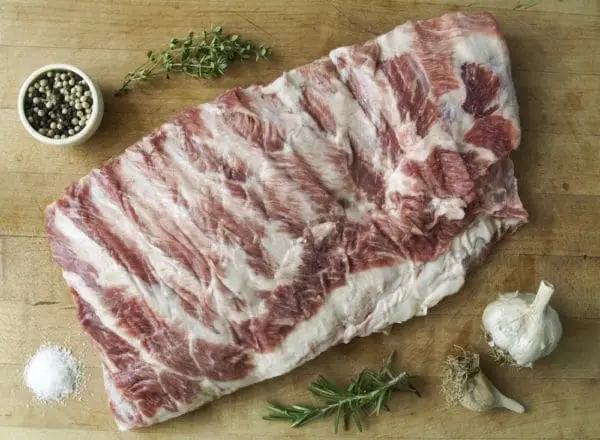 Pasture raised pork spare ribs on a wood cutting board with garnishes and garlic.