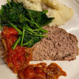 Grass fed beef meatloaf with tomato relish on a plate.