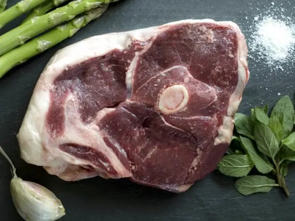 Grass fed lamb leg steak on a slate board with salt and garnishes.