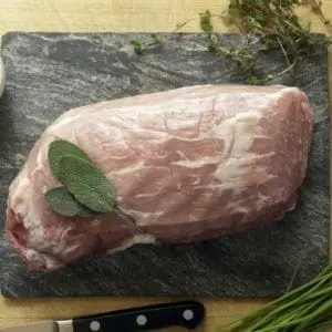 A pasture raised pork eye of round roast on a cutting board with sage and seasonings.