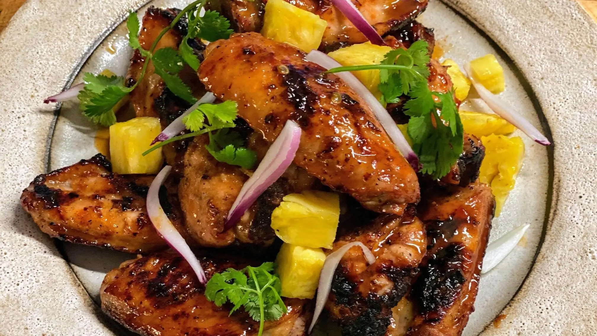 Pasture Raised and Certified Organic chicken wings barbequed served with pineapple and cilantro on a plate.