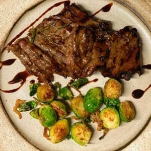Grass fed and grass finished skirt steak from Wrong Direction Farm. Shown roasted with a balsamic glaze on a plate served along with brussels sprouts.
