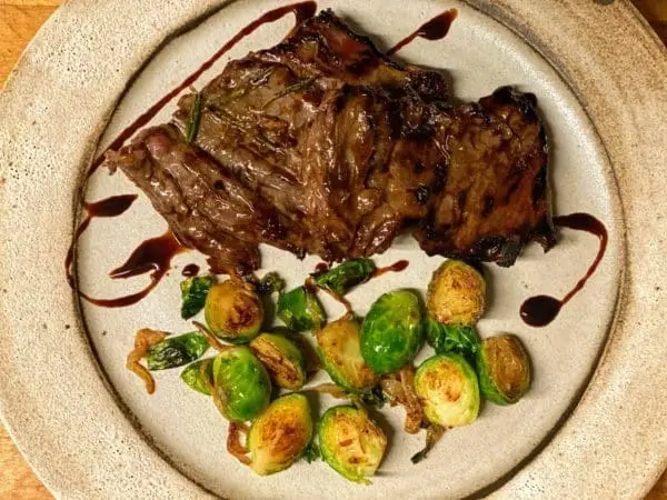 Grass fed and grass finished skirt steak from Wrong Direction Farm. Shown roasted with a balsamic glaze on a plate served along with brussels sprouts.