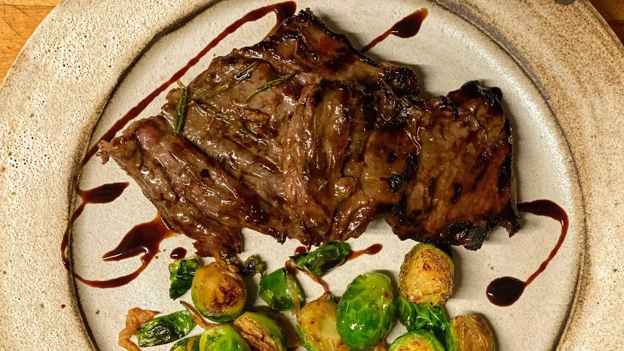 Grass fed and grass finished skirt steak from Wrong Direction Farm. Shown roasted with a balsamic glaze on a plate served along with brussels sprouts.