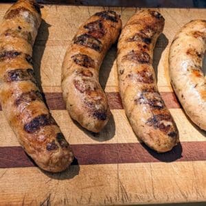 Four grilled mild Italian chicken sausage links from Wrong Direction Farm on a cutting board.