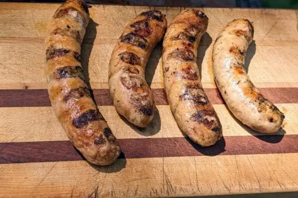 Four grilled mild Italian chicken sausage links from Wrong Direction Farm on a cutting board.