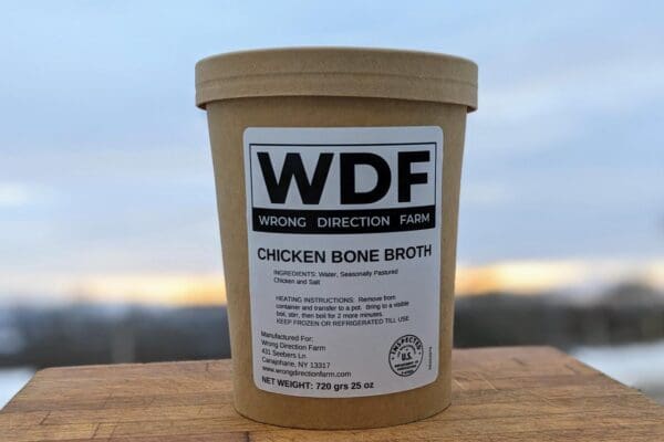 One container of Wrong Direction Farm bone broth on a cutting board with a sunrise sky in the background.