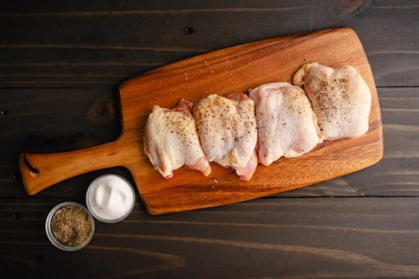 Four boneless Organic, pasture raised chicken thighs from Wrong Direction Farm n a cutting board, dusted with spices before cooking.