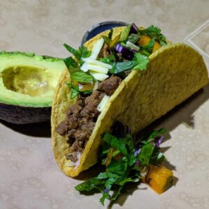 Ancho seasoned grass fed beef served in a hard corn taco shell with rice, chopped vegetables, shredded cheese, and avocado.