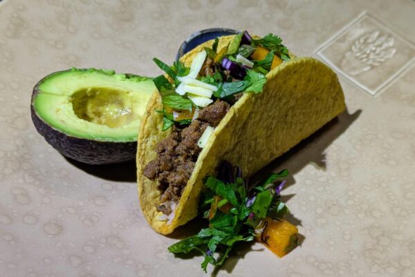 Ancho seasoned grass fed beef served in a hard corn taco shell with rice, chopped vegetables, shredded cheese, and avocado.